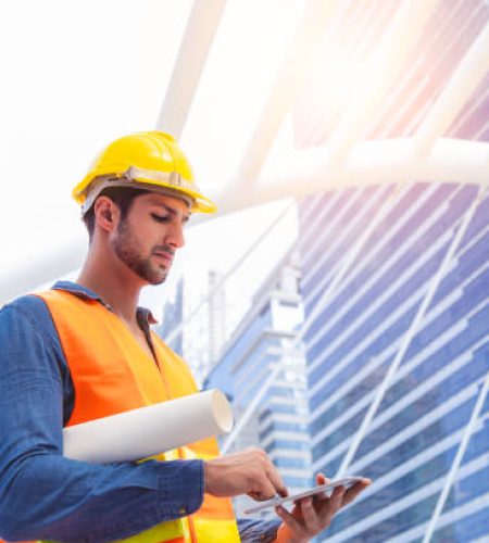 Blue collar worker, engineer man work on digital tablet, hold blue print, wear safety hat, stand near worksite. Worker guy survey a land for big project of building or estate. look determined